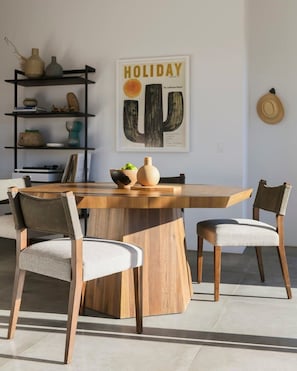 A dining area with a wooden table, four chairs, a vase, and a cactus-themed wall art. - Hightail House By Homestead Modern (Joshua Tree)