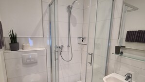 Uma casa de banho moderna com cabine de duche em vidro, sanita, lavatório e espelho.