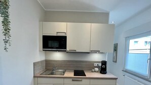 Cozinha moderna com armários brancos, micro-ondas embutido, pia e cafeteira.