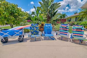 Een rij strandstoelen met een tropisch design, een blauwe kar en een huis op de achtergrond.