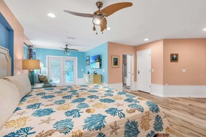 A bedroom with a bed, two ceiling fans, a door, and a wall with a picture.