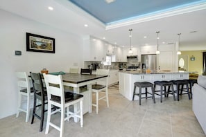 Een moderne keuken met witte kasten, een centraal eiland met barstoelen, en een eethoek met een houten tafel en stoelen.