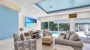 Uma sala de estar ampla, com uma televisão grande, assentos confortáveis e vista para a piscina e área externa.