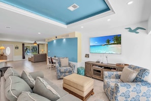 A spacious living room with a large flat-screen TV, comfortable seating, and a view of the outdoors.