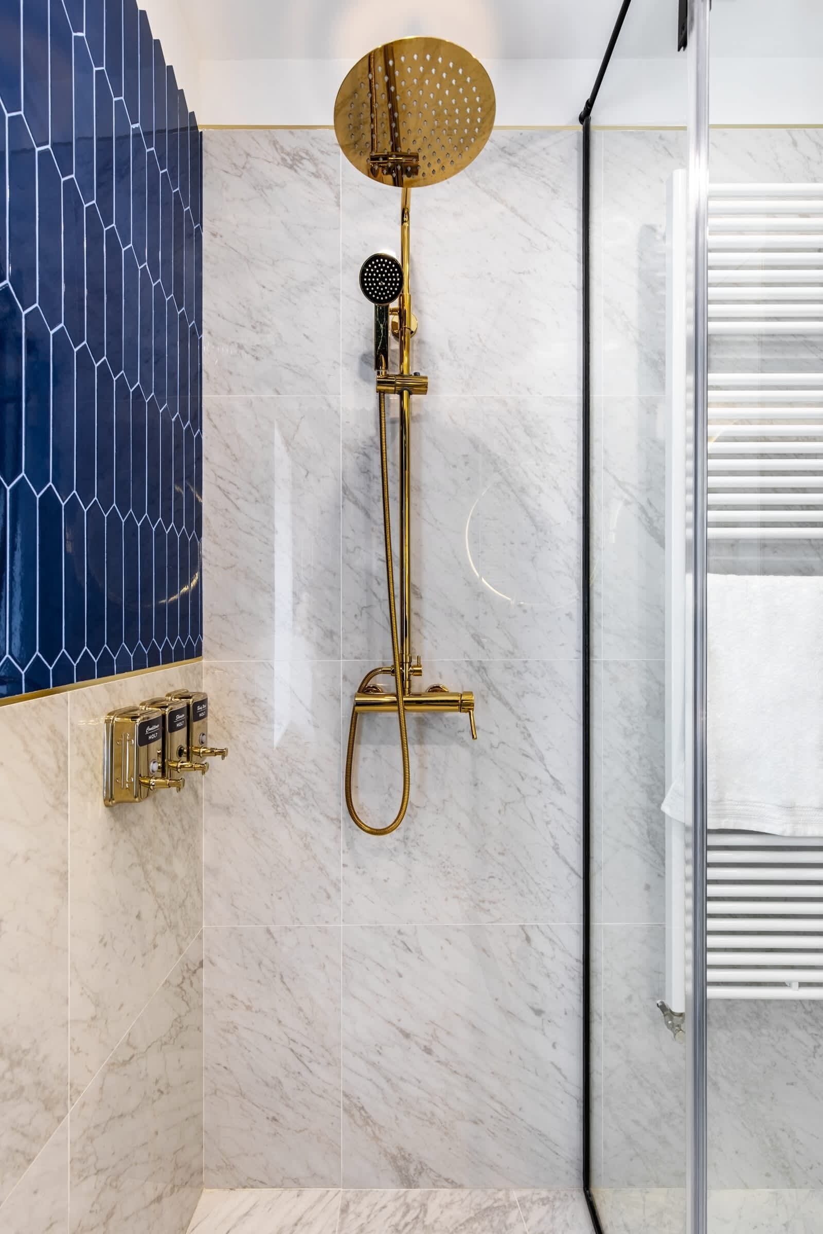 Une salle de bain moderne avec une pomme de douche dorée, des murs en marbre et un mur d’accent orné de carreaux bleus aux motifs géométriques.