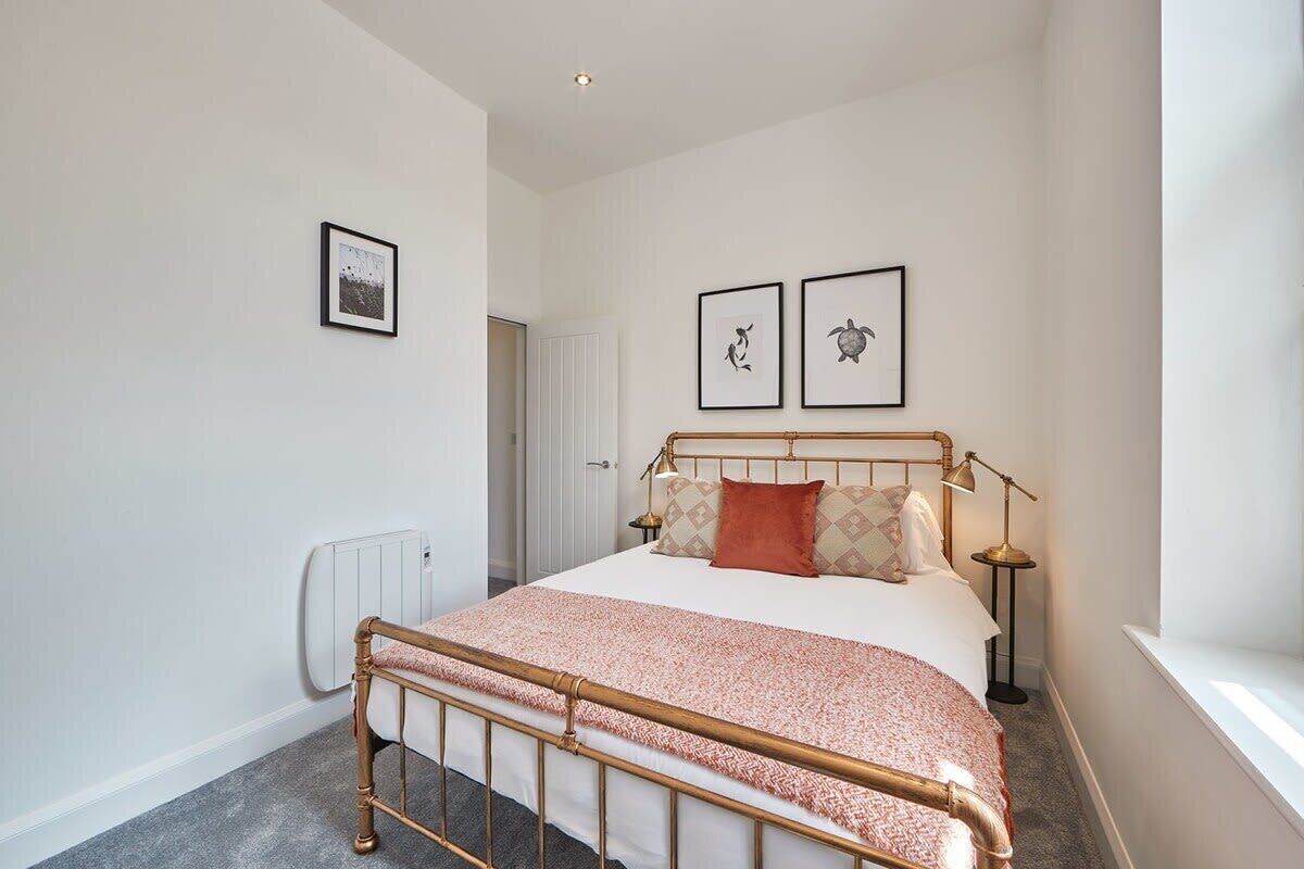 Une chambre à coucher avec un lit, un radiateur, une fenêtre et deux tableaux encadrés accrochés au mur.