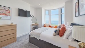A bedroom with a bed, a dresser, a TV, a window with a view, and a framed picture on the wall.