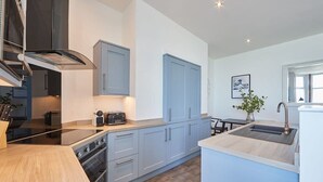 A modern kitchen with grey cabinets, a black range hood, and a wooden countertop.