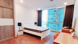 A modern hotel room with a bed, bedside table, lamp, and a view of the city through large windows. - Spacious Modern 4-bed 140sqm Vinhomes Apartment (Ho Chi Minh City)