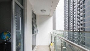 A balcony with a glass railing, a window, and a view of a high-rise building. - Spacious Modern 4-bed 140sqm Vinhomes Apartment (Ho Chi Minh City)