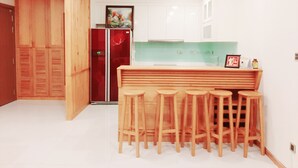 A modern kitchen with white cabinets, a wooden bar counter with stools, and a red refrigerator. - Spacious Modern 4-bed 140sqm Vinhomes Apartment (Ho Chi Minh City)