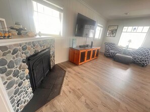 A living room with a stone fireplace, wooden flooring, a TV mounted on the wall, and a patterned sofa.