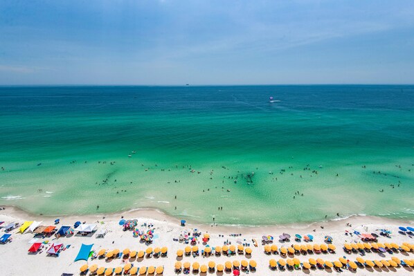 Une plage à l’eau turquoise et limpide, avec un rivage sablonneux, de nombreux parasols et des chaises de plage.