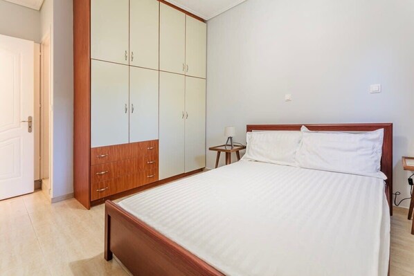 A bedroom with a bed, wooden wardrobe, and a small bedside table.