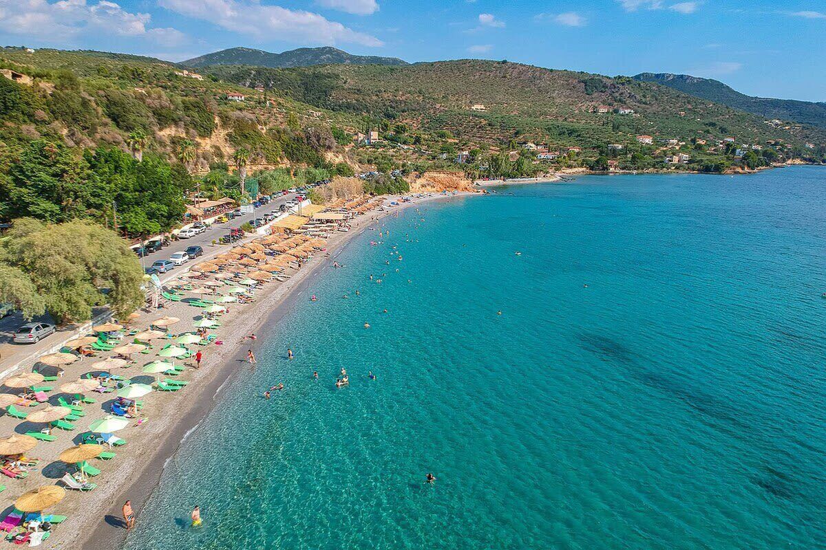 A coastal beach with clear turquoise waters, umbrellas, and people swimming.