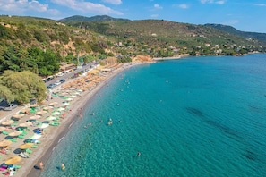 Una playa costera con aguas turquesas cristalinas, sombrillas y gente nadando.