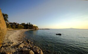 A coastal scene with a pebbly beach, a clear sky, and buildings on the left.