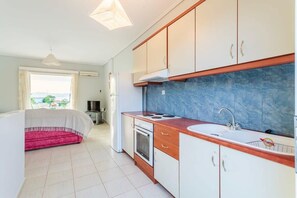 A modern kitchen with white cabinets, a blue backsplash, and a red sofa in the living area.