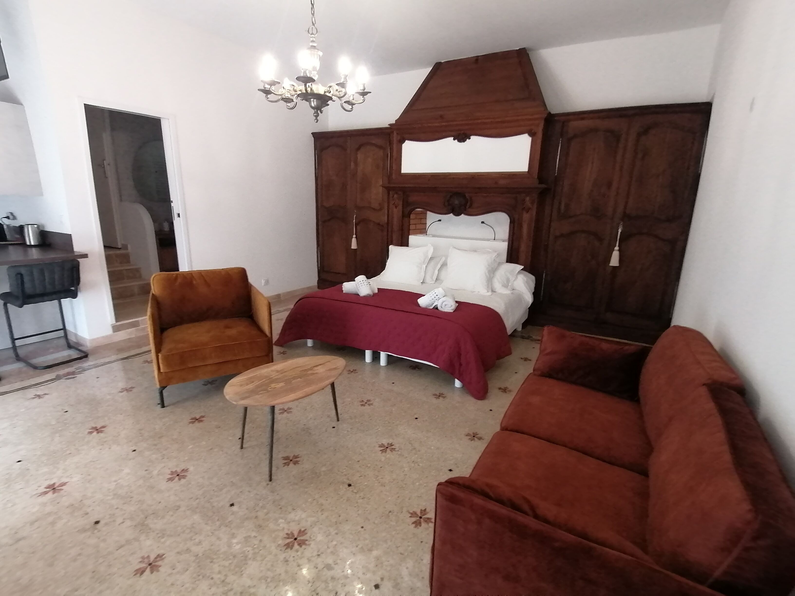 Un dormitorio con cama, dos sillones, una mesita y una araña.