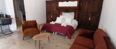Un dormitorio con cama, dos sillones, una mesita y una araña.