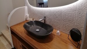Ett badrum med ett handfat i trä, en svart tvättställ och en stor spegel med en dekorativ ram.