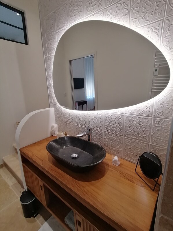 Un baño con tocador de madera, un lavamanos negro y un espejo grande con marco decorativo.
