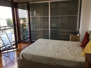A bedroom with a bed, a nightstand, a lamp, a sliding glass door, and a view of the outside.