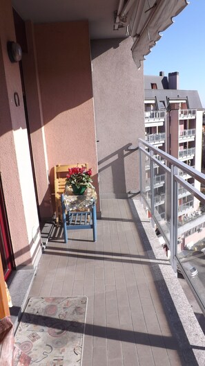 A balcony with a chair, a small table with flowers, and a view of adjacent buildings.
