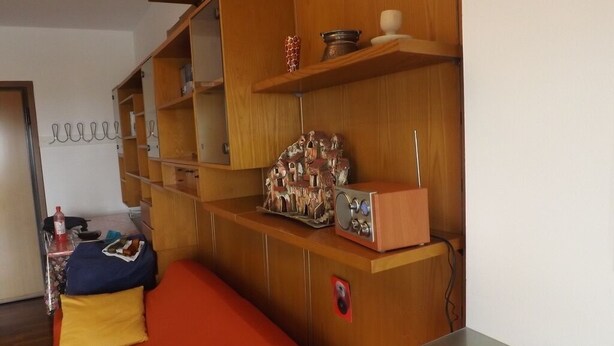 Ein Zimmer mit einem Holzkasten, einem roten Sofa und einem kleinen Tisch.