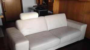 A beige leather sofa in a room with wooden flooring and a wooden cabinet in the background. - appartamento luminoso  con balcone, silenzioso davanti a un parco vicino a GYM (Gallarate)