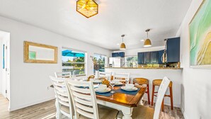 A dining area with a wooden table, white chairs, and a view of the outdoors. - Chic Pool Home Steps to Beach! Game Room and Paddleboards (Holmes Beach)