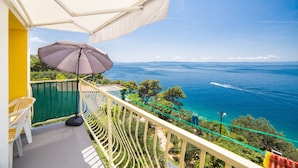 Un balcon avec un parasol blanc, une chaise et une vue sur la mer.