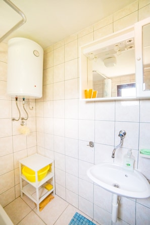 A bathroom with a white sink, a mirror, a yellow shelf, and a white toilet.