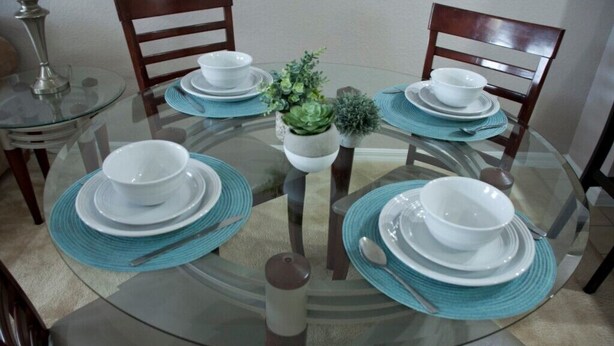 A round glass dining table with white plates and blue placemats, surrounded by wooden chairs. - Venetian Bay Townhome 3 Bedroom Townhouse by RedAwning (Kissimmee)