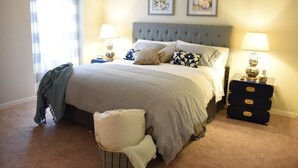 Une chambre à coucher bien rangée, avec un grand lit, deux tables de chevet avec des lampes, une commode et deux tableaux encadrés accrochés au mur.