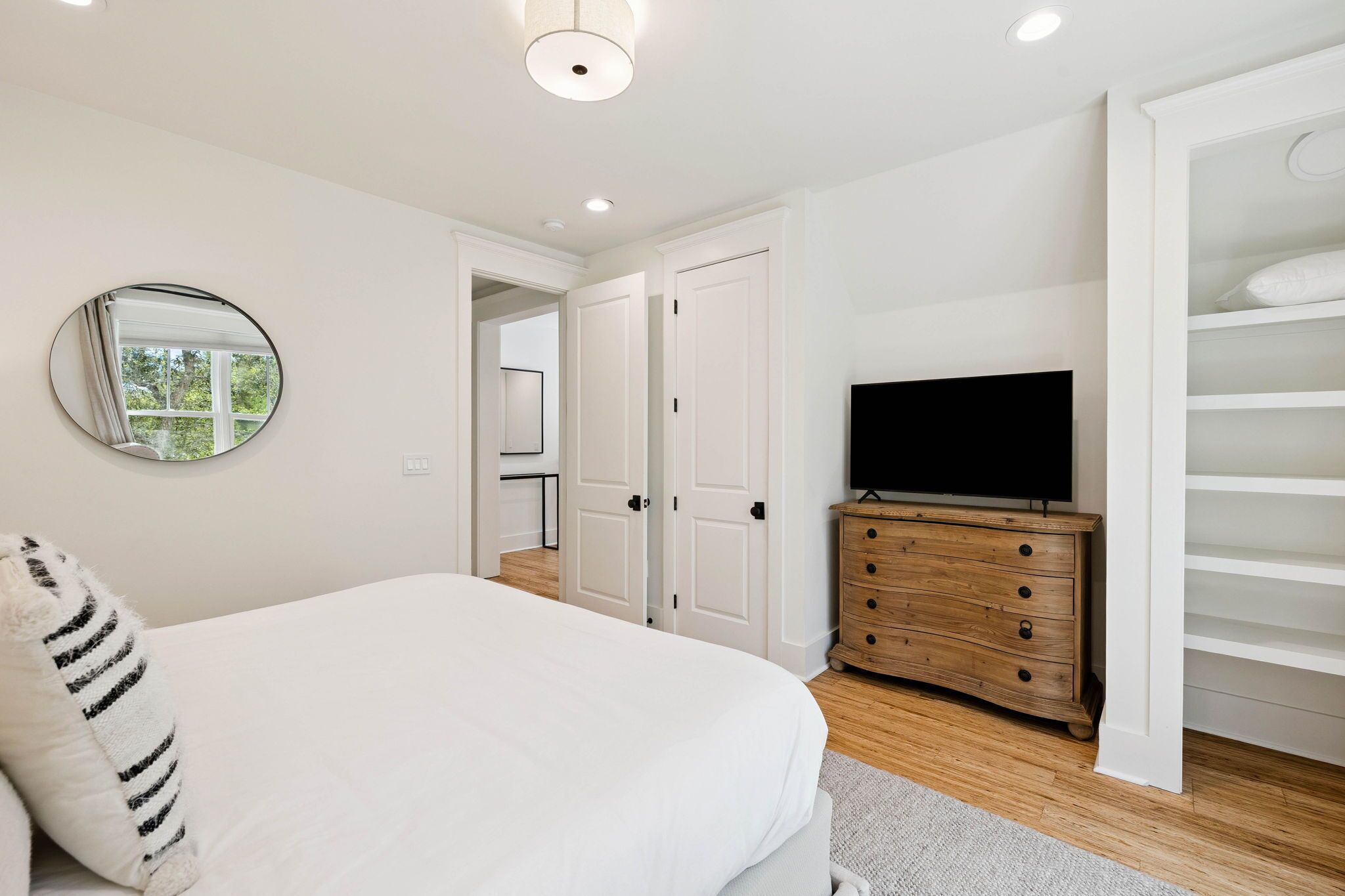 A bedroom with a bed, a dresser, a television, and a walk-in closet.