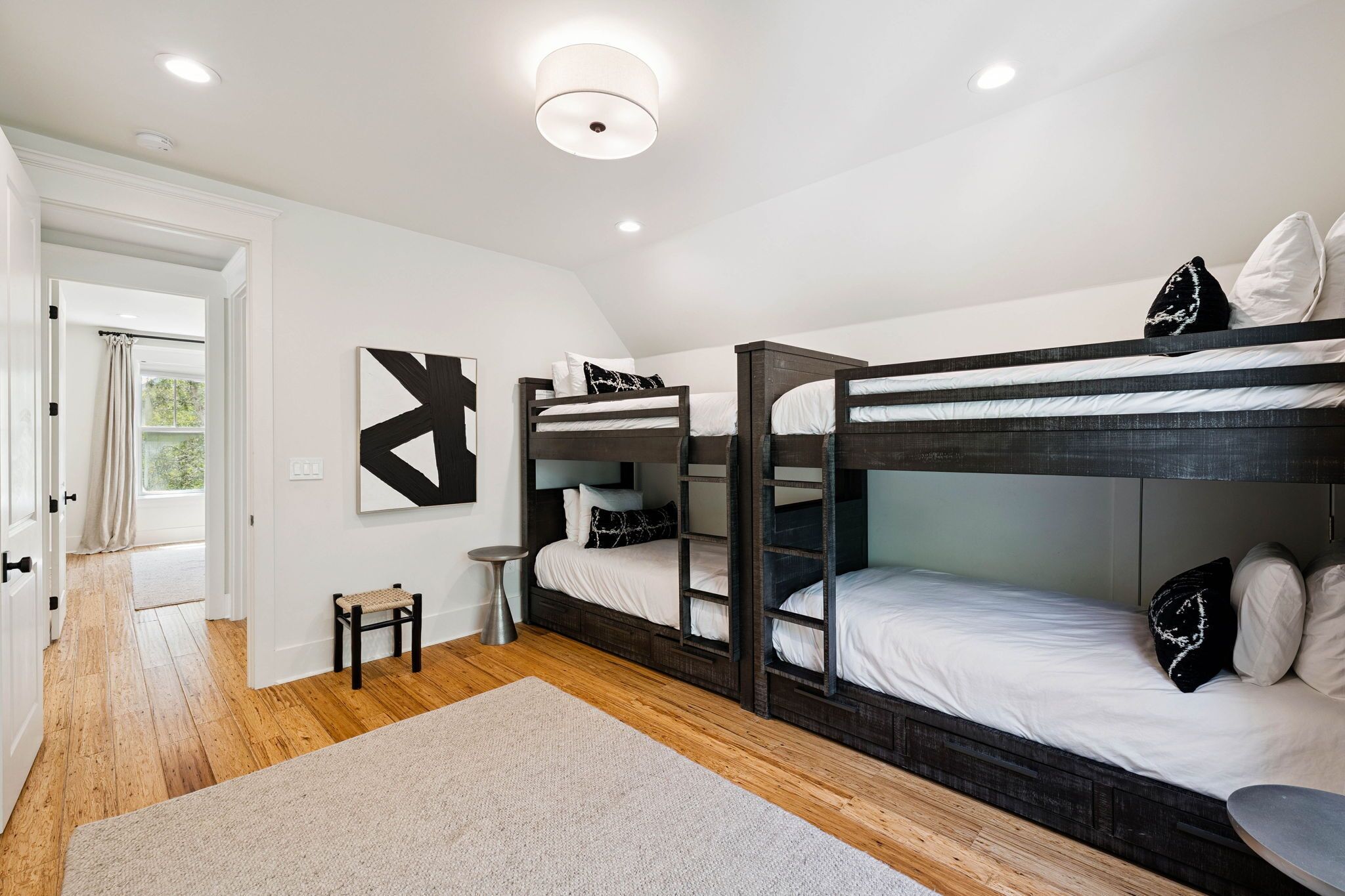 A bunk bed room with a wooden floor, a small bench, a round table, and a large abstract painting on the wall.