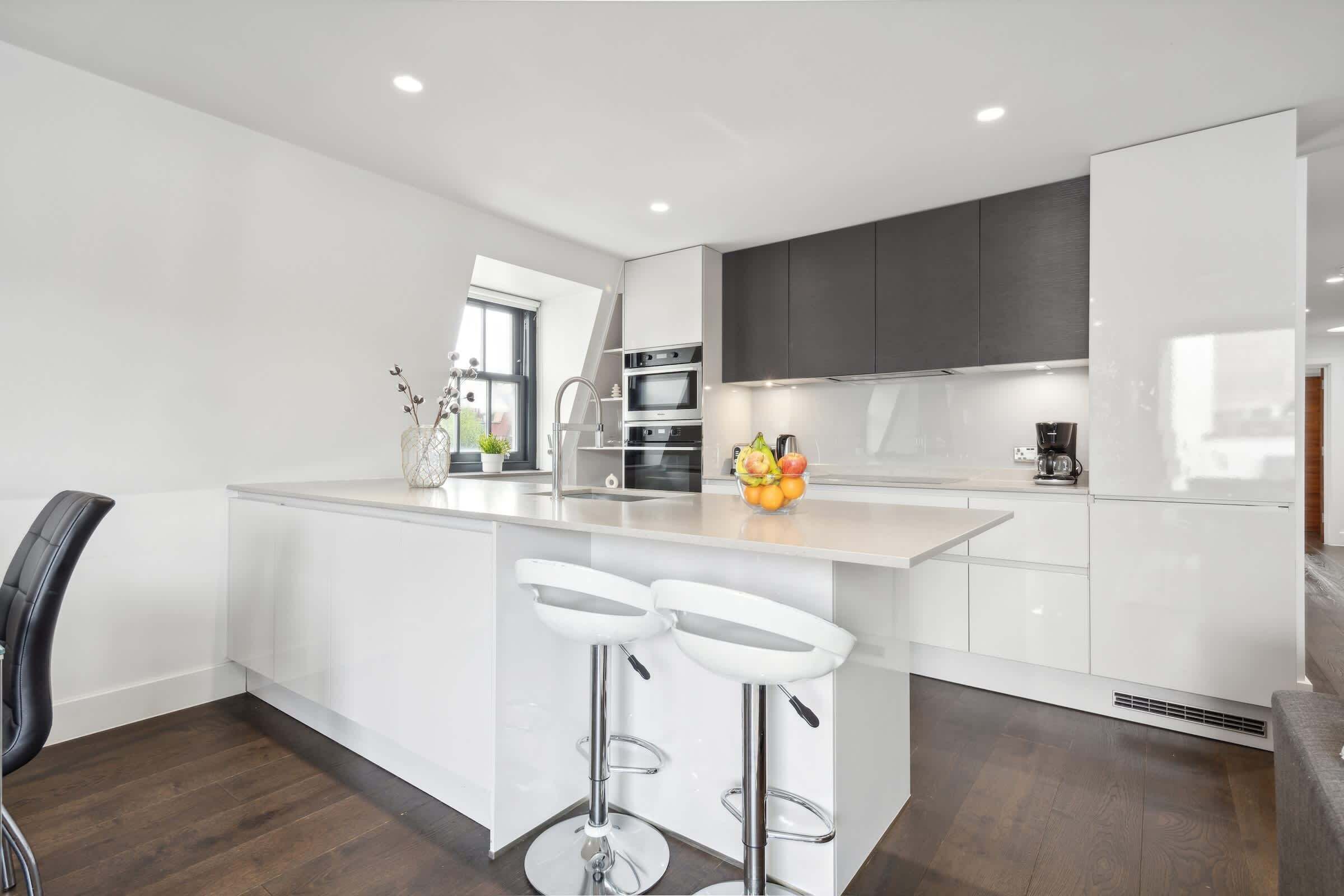 Een moderne keuken met witte kasten, een centraal eiland met barstoelen, een ingebouwde oven en een koffieapparaat.