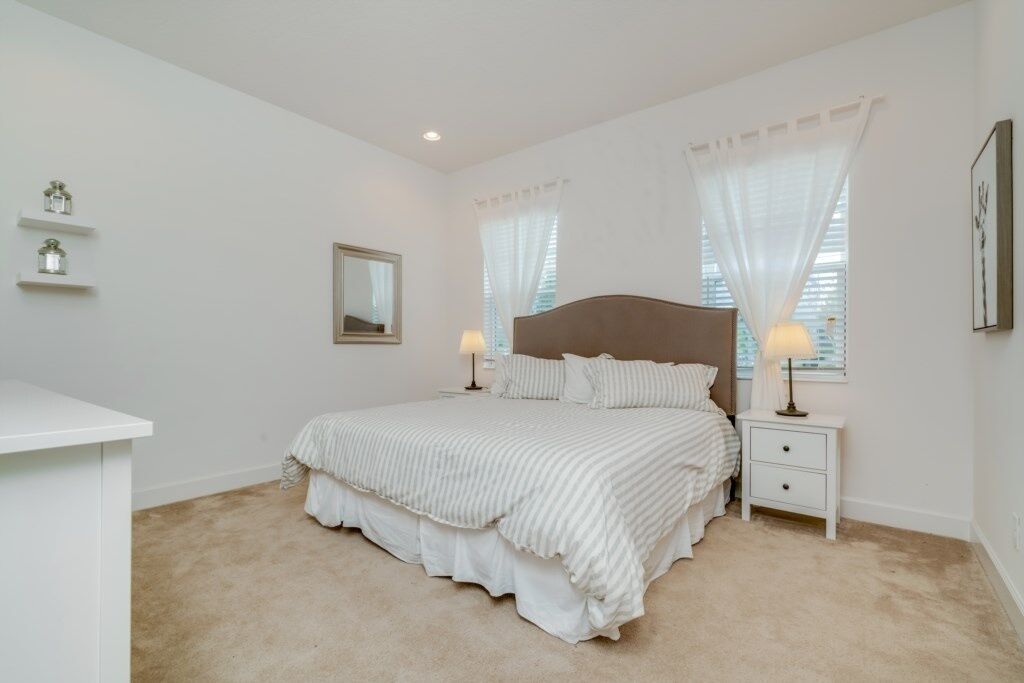 Un dormitorio con cama, mesitas de noche, un espejo y una ventana con cortinas.