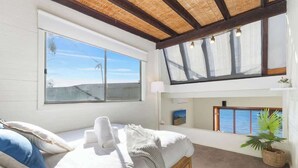 A bedroom with a large window, a bed with pillows, a bedside lamp, and a potted plant. - Scotland Island Waterfront House w/ Private Jetty (Scotland Island)