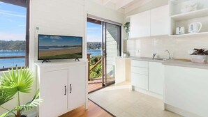 A modern kitchen with a TV, white cabinets, and a view of the sea. - Scotland Island Waterfront House w/ Private Jetty (Scotland Island)