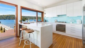 A modern kitchen with a large island, white cabinets, and a view of the water. - Scotland Island Waterfront House w/ Private Jetty (Scotland Island)