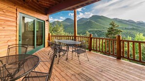 Una terraza de madera con una mesa y sillas, con vista a un paisaje montañoso.