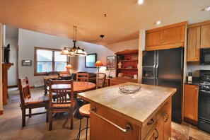 A kitchen with wooden cabinets, a black refrigerator, a dining area with chairs and a table, and pendant lighting.