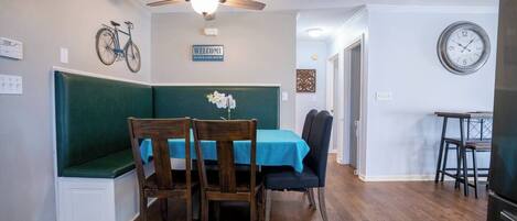 A dining area with a table set for two, a bench, and a ceiling fan.
