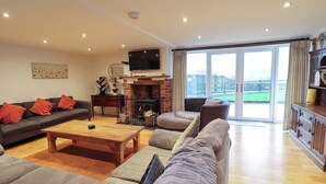 A spacious living room with a fireplace, a television, and a large window offering a view of the outdoors. - Bwthyn Y Bugail (shepherd's Cottage (Oswestry)