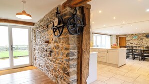 A spacious kitchen with a stone wall, wooden beams, and a large dining area with multiple chairs. - Bwthyn Y Bugail (shepherd's Cottage (Oswestry)