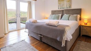 A bedroom with a large bed, a view through a sliding door, and a painting on the wall. - Bwthyn Y Bugail (shepherd's Cottage (Oswestry)