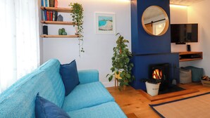 A modern living room with a blue sofa, a fireplace, a television, and bookshelves with plants. - Estuary View (Newquay)