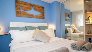 A neatly made bed with white and beige bedding, a wooden wall art piece, and a bedside lamp. - Estuary View (Newquay)